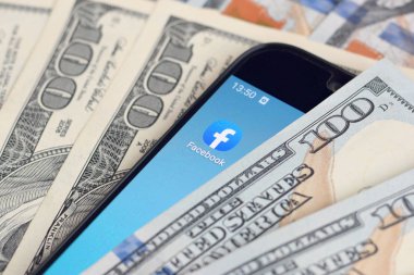 Kharkov, Ukrayna - 6 Şubat 2020: Facebook uygulamalı akıllı telefon ekranı ve bir sürü yüz dolarlık banknot. İş ve sosyal ağ kavramı