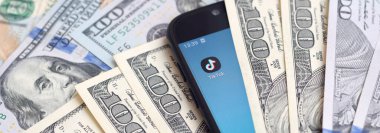 Kharkov, Ukrayna - 6 Şubat 2020: Tiktok uygulamalı akıllı telefon ekranı ve bir sürü yüz dolarlık banknot. İş ve sosyal ağ kavramı