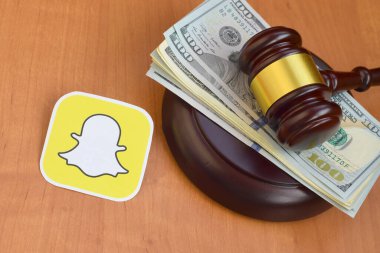 KHARKOV, UKRAINE - FEBRUARY 17, 2020: Snapchat paper logo lies with judge gavel and hundred dollar bills. Entertainment lawsuit concept
