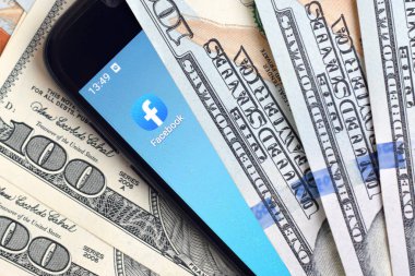 Kharkov, Ukrayna - 6 Şubat 2020: Facebook uygulamalı akıllı telefon ekranı ve bir sürü yüz dolarlık banknot. İş ve sosyal ağ kavramı