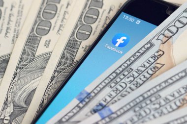 Kharkov, Ukrayna - 6 Şubat 2020: Facebook uygulamalı akıllı telefon ekranı ve bir sürü yüz dolarlık banknot. İş ve sosyal ağ kavramı