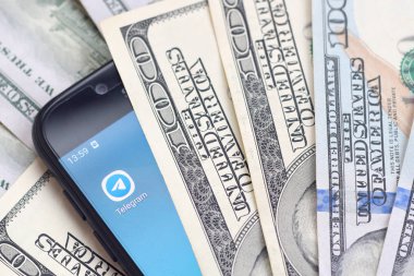 Kharkov, Ukrayna - 6 Şubat 2020: Telgraf uygulamalı akıllı telefon ekranı ve bir sürü yüz dolarlık banknot. İş ve sosyal ağ kavramı