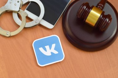 Kharkov, Ukrayna - 17 Şubat 2020: Vkontakte kağıt logosu ahşap yargıç tokmağı, akıllı telefon ve kelepçeli. Eğlence davaları konsepti