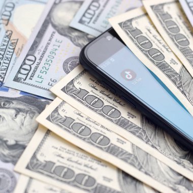 Kharkov, Ukrayna - 6 Şubat 2020: Tiktok uygulamalı akıllı telefon ekranı ve bir sürü yüz dolarlık banknot. İş ve sosyal ağ kavramı