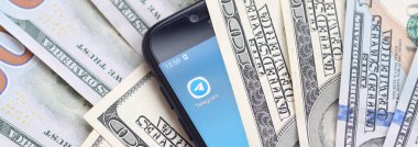 Kharkov, Ukrayna - 6 Şubat 2020: Telgraf uygulamalı akıllı telefon ekranı ve bir sürü yüz dolarlık banknot. İş ve sosyal ağ kavramı