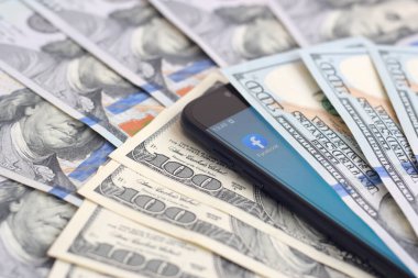 Kharkov, Ukrayna - 6 Şubat 2020: Facebook uygulamalı akıllı telefon ekranı ve bir sürü yüz dolarlık banknot. İş ve sosyal ağ kavramı