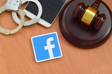 Kharkov, Ukrayna - 17 Şubat 2020: Facebook kağıt logosu ahşap yargıç tokmağı, akıllı telefon ve kelepçeli. Eğlence davaları konsepti