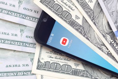 Kharkov, Ukrayna - 6 Şubat 2020: Youtube uygulamalı akıllı telefon ekranı ve bir sürü yüz dolarlık banknotlar. İş ve sosyal ağ kavramı