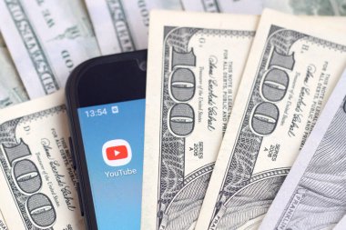 Kharkov, Ukrayna - 6 Şubat 2020: Youtube uygulamalı akıllı telefon ekranı ve bir sürü yüz dolarlık banknotlar. İş ve sosyal ağ kavramı