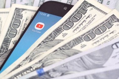 Kharkov, Ukrayna - 6 Şubat 2020: Youtube uygulamalı akıllı telefon ekranı ve bir sürü yüz dolarlık banknotlar. İş ve sosyal ağ kavramı