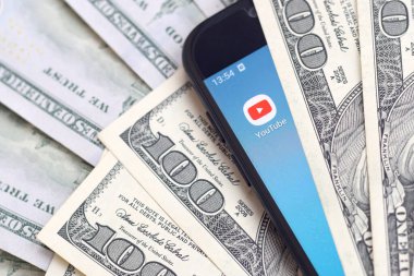 Kharkov, Ukrayna - 6 Şubat 2020: Youtube uygulamalı akıllı telefon ekranı ve bir sürü yüz dolarlık banknotlar. İş ve sosyal ağ kavramı