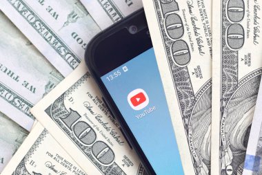 Kharkov, Ukrayna - 6 Şubat 2020: Youtube uygulamalı akıllı telefon ekranı ve bir sürü yüz dolarlık banknotlar. İş ve sosyal ağ kavramı
