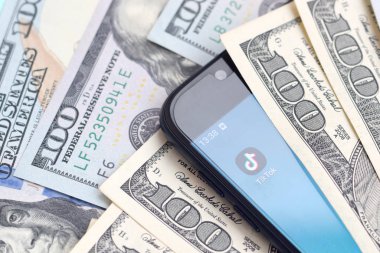 Kharkov, Ukrayna - 6 Şubat 2020: Tiktok uygulamalı akıllı telefon ekranı ve bir sürü yüz dolarlık banknot. İş ve sosyal ağ kavramı