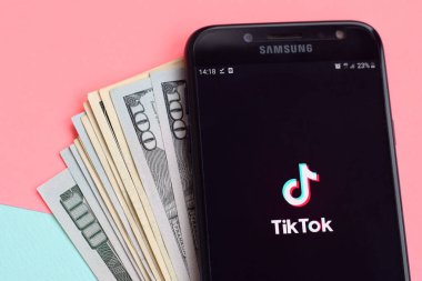 Kharkov, Ukrayna - 16 Şubat 2020: Samsung akıllı telefon ekranı ve dolar banknotlarında Tiktok uygulaması. Tiktok Bytedance 'in sahip olduğu popüler bir video paylaşım sosyal ağ hizmetidir.