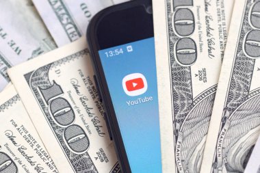 Kharkov, Ukrayna - 6 Şubat 2020: Youtube uygulamalı akıllı telefon ekranı ve bir sürü yüz dolarlık banknotlar. İş ve sosyal ağ kavramı