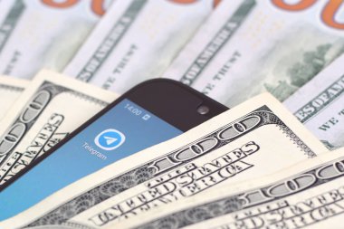 Kharkov, Ukrayna - 6 Şubat 2020: Telgraf uygulamalı akıllı telefon ekranı ve bir sürü yüz dolarlık banknot. İş ve sosyal ağ kavramı