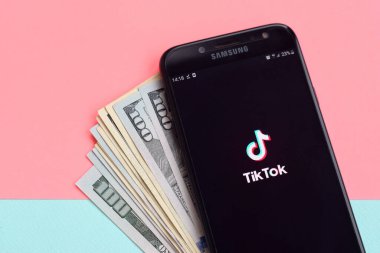 Kharkov, Ukrayna - 16 Şubat 2020: Samsung akıllı telefon ekranı ve dolar banknotlarında Tiktok uygulaması. Tiktok Bytedance 'in sahip olduğu popüler bir video paylaşım sosyal ağ hizmetidir.