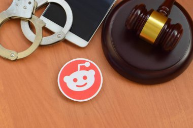 Kharkov, Ukrayna - 17 Şubat 2020: Ahşap yargıç tokmağı, akıllı telefon ve kelepçeli Reddit kağıt logosu. Eğlence davaları konsepti