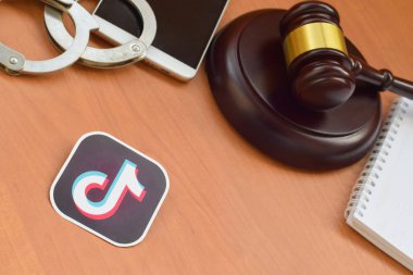 Kharkov, Ukrayna - 17 Şubat 2020: Tiktok kağıt logosu ahşap yargıç tokmağı, akıllı telefon ve kelepçeli. Eğlence davaları konsepti