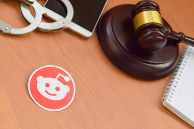 Kharkov, Ukrayna - 17 Şubat 2020: Ahşap yargıç tokmağı, akıllı telefon ve kelepçeli Reddit kağıt logosu. Eğlence davaları konsepti