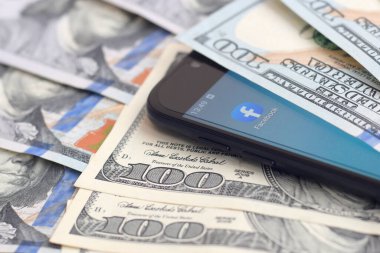 Kharkov, Ukrayna - 6 Şubat 2020: Facebook uygulamalı akıllı telefon ekranı ve bir sürü yüz dolarlık banknot. İş ve sosyal ağ kavramı