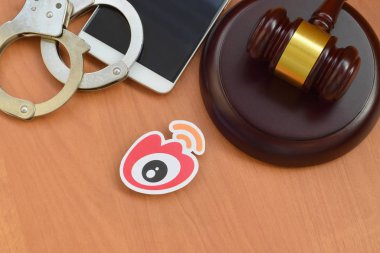 Kharkov, Ukrayna - 17 Şubat 2020: Weibo kağıt logosu ahşap yargıç tokmağı, akıllı telefon ve kelepçeli. Eğlence davaları konsepti