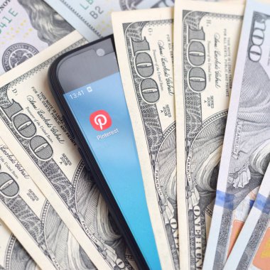Kharkov, Ukrayna - 6 Şubat 2020: Pinterest uygulamalı akıllı telefon ekranı ve bir sürü yüz dolarlık banknot. İş ve sosyal ağ kavramı
