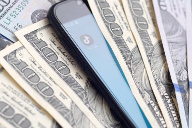 Kharkov, Ukrayna - 6 Şubat 2020: Tiktok uygulamalı akıllı telefon ekranı ve bir sürü yüz dolarlık banknot. İş ve sosyal ağ kavramı