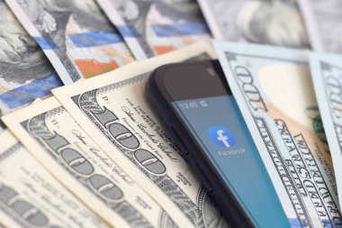 Kharkov, Ukrayna - 6 Şubat 2020: Facebook uygulamalı akıllı telefon ekranı ve bir sürü yüz dolarlık banknot. İş ve sosyal ağ kavramı