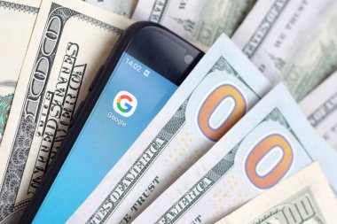 Kharkov, Ukrayna - 6 Şubat 2020: Google uygulamalı akıllı telefon ekranı ve bir sürü yüz dolarlık banknot. İş ve sosyal ağ kavramı