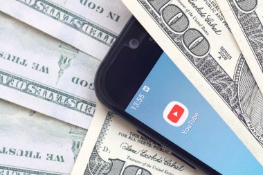 Kharkov, Ukrayna - 6 Şubat 2020: Youtube uygulamalı akıllı telefon ekranı ve bir sürü yüz dolarlık banknotlar. İş ve sosyal ağ kavramı