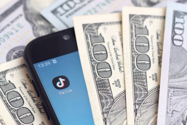 Kharkov, Ukrayna - 6 Şubat 2020: Tiktok uygulamalı akıllı telefon ekranı ve bir sürü yüz dolarlık banknot. İş ve sosyal ağ kavramı