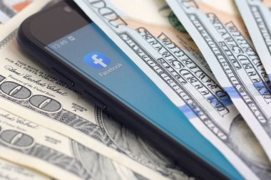 Kharkov, Ukrayna - 6 Şubat 2020: Facebook uygulamalı akıllı telefon ekranı ve bir sürü yüz dolarlık banknot. İş ve sosyal ağ kavramı