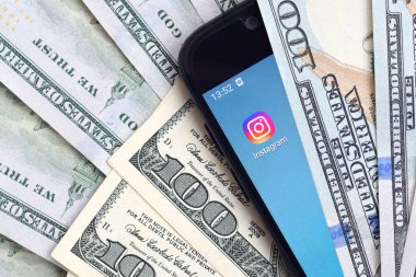 Kharkov, Ukrayna - 6 Şubat 2020: Instagram uygulamalı akıllı telefon ekranı ve bir sürü yüz dolarlık banknot. İş ve sosyal ağ kavramı