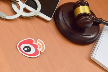 Kharkov, Ukrayna - 17 Şubat 2020: Weibo kağıt logosu ahşap yargıç tokmağı, akıllı telefon ve kelepçeli. Eğlence davaları konsepti