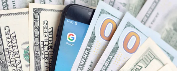 Kharkov, Ukrayna - 6 Şubat 2020: Google uygulamalı akıllı telefon ekranı ve bir sürü yüz dolarlık banknot. İş ve sosyal ağ kavramı