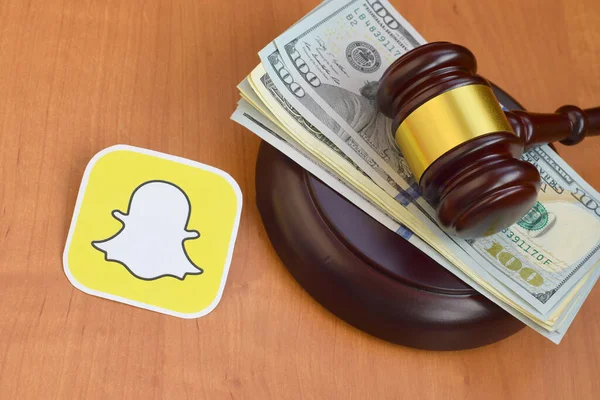 KHARKOV, UKRAINE - FEBRUARY 17, 2020: Snapchat paper logo lies with judge gavel and hundred dollar bills. Entertainment lawsuit concept