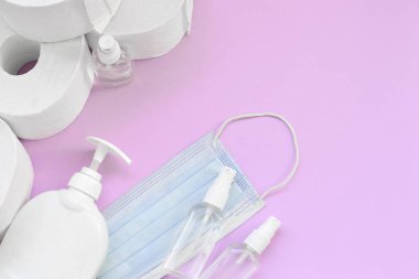 Covid-19 karantina saatleri için önemli eşyalar. Ameliyat maskeli tuvalet kağıdı ve eflatun kaplamalı sıvı sabun şişeli el dezenfektanı. Hijyen ve sağlık hizmetleri kavramı