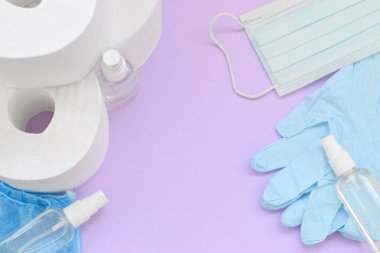 Covid-19 karantina saatleri için önemli eşyalar. Tuvalet kağıdı, plastik tek kullanımlık eldivenler, ameliyat maskesi ve eflatun arka planda el dezenfektanı.