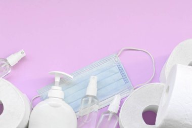 Covid-19 karantina saatleri için önemli eşyalar. Ameliyat maskeli tuvalet kağıdı ve eflatun kaplamalı sıvı sabun şişeli el dezenfektanı. Hijyen ve sağlık hizmetleri kavramı