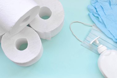 Covid-19 karantina saatleri için önemli eşyalar. Tuvalet kağıdı, plastik tek kullanımlık eldivenler, ameliyat maskesi ve mavi arka planda sıvı sabun şişesi. Sağlık ve hijyen konsepti