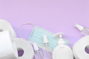 Covid-19 karantina saatleri için önemli eşyalar. Ameliyat maskeli tuvalet kağıdı ve eflatun kaplamalı sıvı sabun şişeli el dezenfektanı. Hijyen ve sağlık hizmetleri kavramı