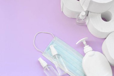 Covid-19 karantina saatleri için önemli eşyalar. Ameliyat maskeli tuvalet kağıdı ve eflatun kaplamalı sıvı sabun şişeli el dezenfektanı. Hijyen ve sağlık hizmetleri kavramı