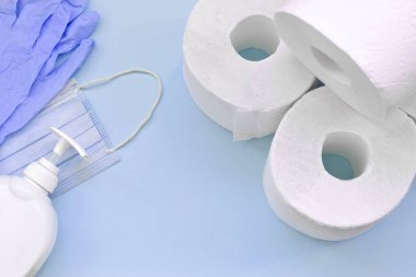 Covid-19 karantina saatleri için önemli eşyalar. Tuvalet kağıdı, plastik tek kullanımlık eldivenler, ameliyat maskesi ve mavi arka planda sıvı sabun şişesi. Sağlık ve hijyen konsepti
