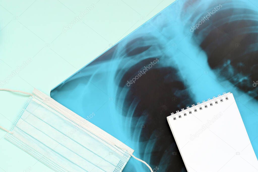 Respiratory mask and empty notepad page on x-ray of human lungs, top view. Coronavirus Covid-19 pneumonia concept.