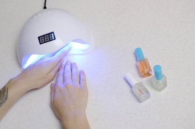 Manikür prosedüründeki genç bir kadının elleri beyaz arka plana yaklaşır. Kadın Oje Süreci. Hızlı kurumak için kabuklu lamba kullanan bir kadın.