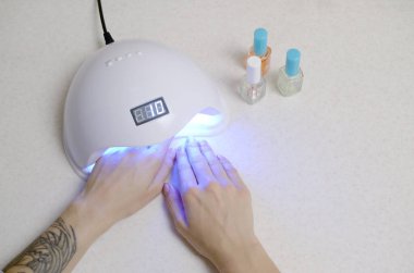 Manikür prosedüründeki genç bir kadının elleri beyaz arka plana yaklaşır. Kadın Oje Süreci. Hızlı kurumak için kabuklu lamba kullanan bir kadın.