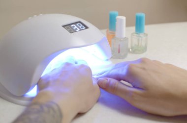 Manikür prosedüründeki genç bir kadının elleri beyaz arka plana yaklaşır. Kadın Oje Süreci. Hızlı kurumak için kabuklu lamba kullanan bir kadın.