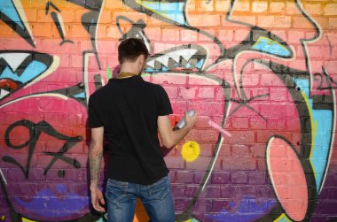 Sırt çantası ve gaz maskesi takan genç grafiti sanatçısı, tuğla duvara pembe tonlarda grafiti yapıyor. Sokak sanatı ve çağdaş boyama süreci. Gençlik alt kültüründe eğlence