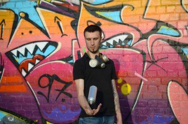 Boynunda gaz maskesi olan genç bir grafiti sanatçısı sprey kutusunu renkli pembe duvar yazısına fırlatıyor. Sokak sanatı ve çağdaş boyama süreci. Gençlik alt kültüründe eğlence